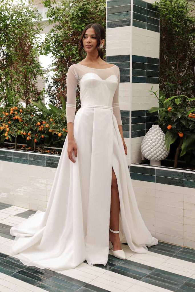 In questa foto una modella indossa un abito ad A con scollo a cuore e coprispalle a maniche lunghe in tulle della collezione Mariù di Atelier Benedetta