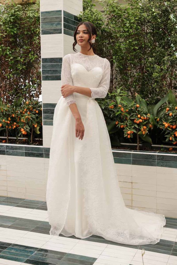 In questa foto una modella indossa un abito da sposa in organza con capospalla in pizzo chantilly della collezione Mariù di Atelier Benedetta
