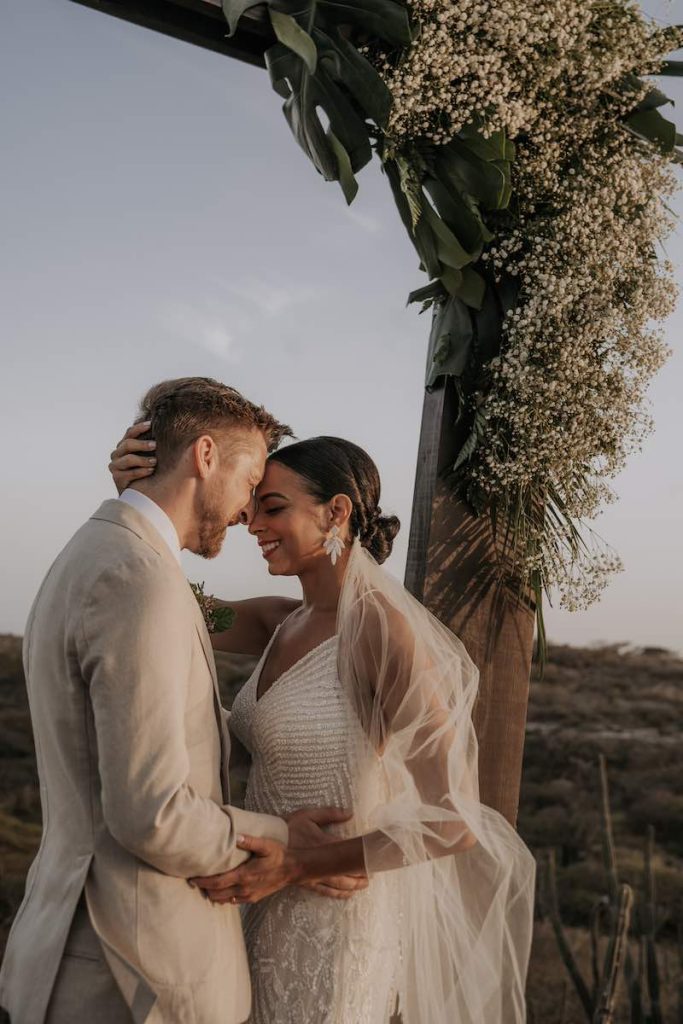 In questa foto due sposi abbracciati davanti ad un arco di legno decorato con gypsophila di colore bianco