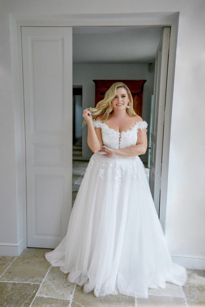 In questa foto una modella plus size indossa un abito da sposa della collezione Sincerity Bridal Primavera Estate 2025 con corpetto con fiori 3D e gonna in tulle