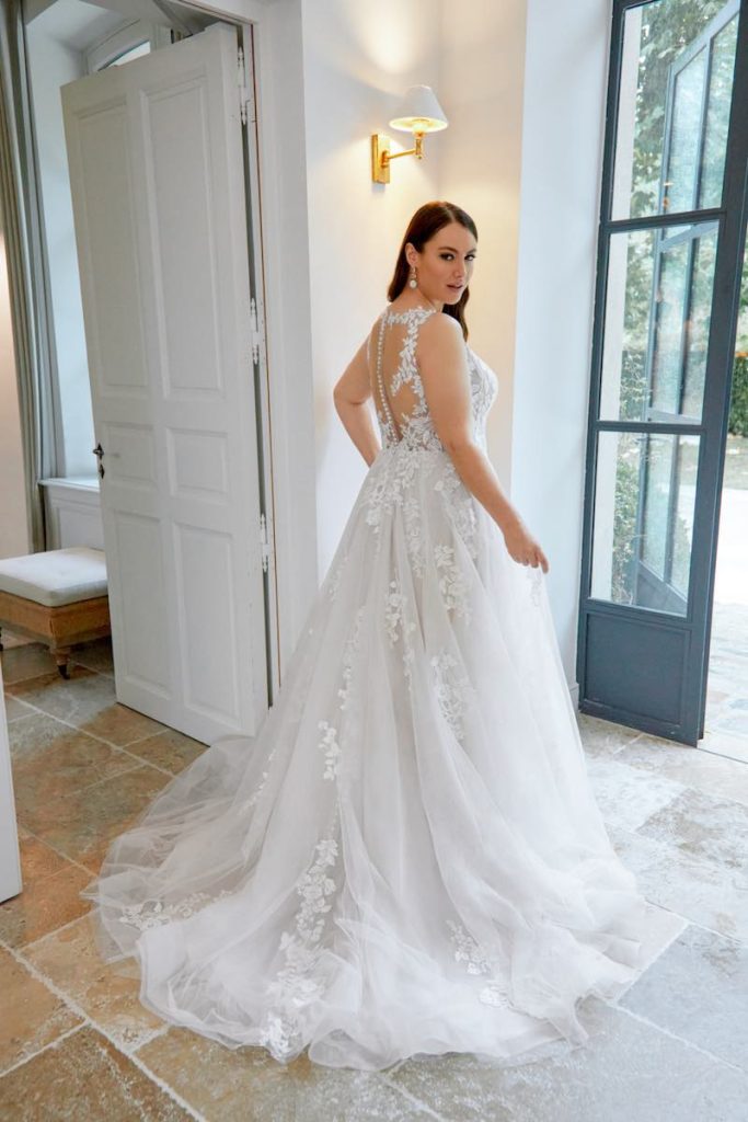 In questa foto una modella plus size  indossa un abito da sposa ampio in tulle e pizzo con lungo strascico