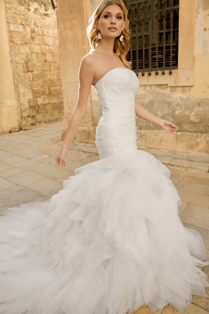 In questa foto una modella indossa un abito da sposa semi sirena in tulle e gonna con ruches della collezione Sincerity Bridal Primavera Estate 2025