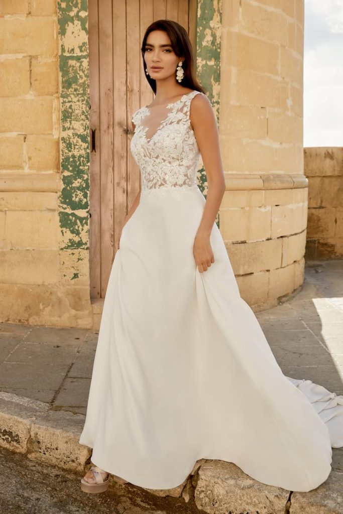In questa foto una modella indossa un abito da sposa della collezione Sincerity Bridal Primavera Estate 2025 con corpetto in pizzo ricamato, scollo a V e gonna in crêpe