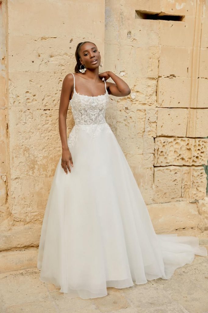 In questa foto una modella indossa un abito da sposa ad A della collezione Sincerity Bridal Primavera Estate 2025 con corpetto in pizzo, scollatura quadrata e gonna in organza