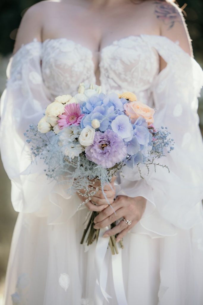 In questa foto, un bouquet da sposa 2025 nei toni del rosa pesca, del lilla, del celeste e del bianco