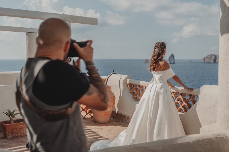 In questa foto Salvatore Cimino di spalle mentre fotografa una sposa di spalle mentre guarda il mare da una terrazza