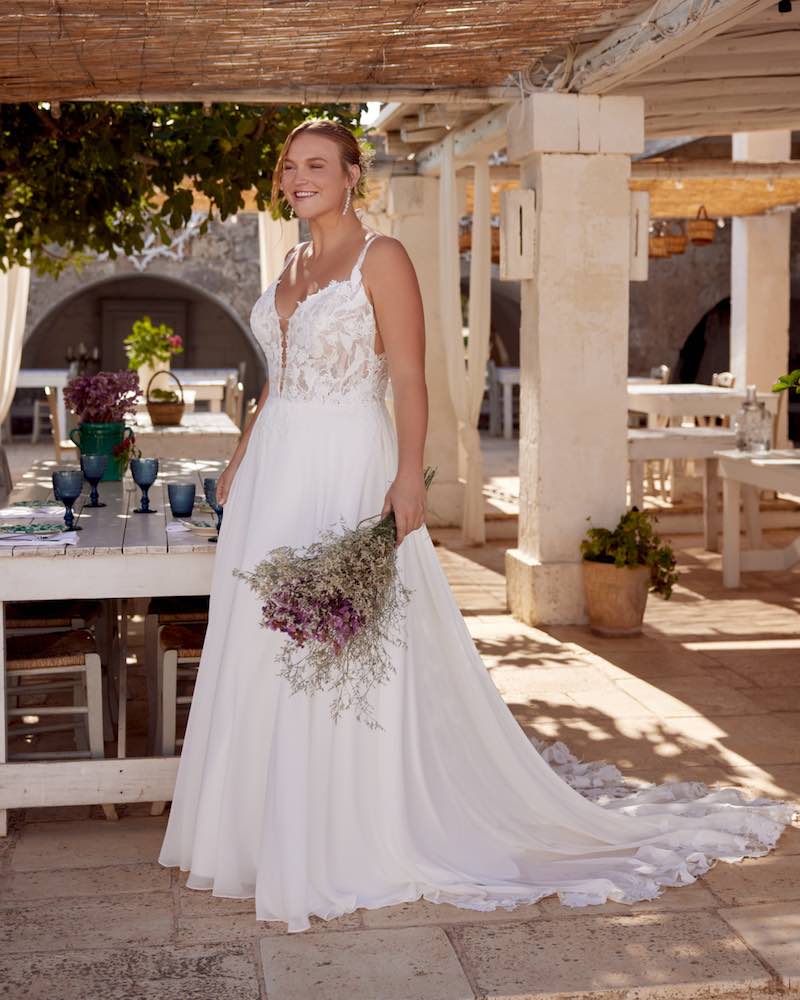 In questa foto, una modella indossa un abito scivolato con corpetto in pizzo e gonna in chiffon della collezione sposa Lilian West SS 2025