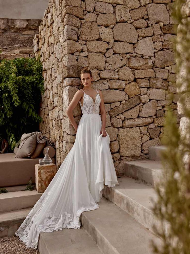 In questa foto, una modella indossa un abito scivolato con corpetto in pizzo e gonna in chiffon della collezione sposa Lilian West SS 2025