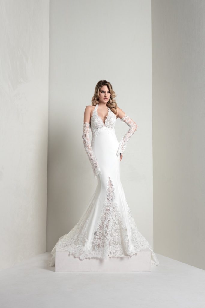 In questa foto, una modella indossa un abito della collezione sposa Markisa 2026 a sirena, in pizzo e crepe con scollatura all'americana e  manicotti staccabili abbinati