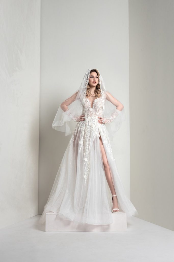 In questa foto, una modella indossa un abito della collezione sposa Markisa 2026 ad A con spacco, in tulle e inserti floreali e velo abbinato