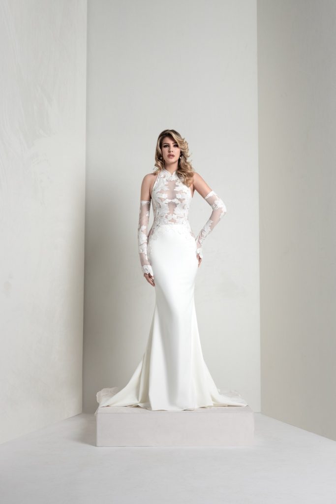 In questa foto, una modella indossa un abito della collezione sposa Markisa 2026 a sirena, con corpetto in pizzo floreale effetto tattoo e manicotti staccabili abbinati