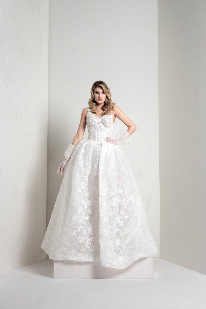 In questa foto, una modella indossa un abito della collezione sposa Markisa 2026 principessa,in pizzo floreale effetto glitter, bustier steccato, scollo a cuore e manicotti staccabili abbinati
