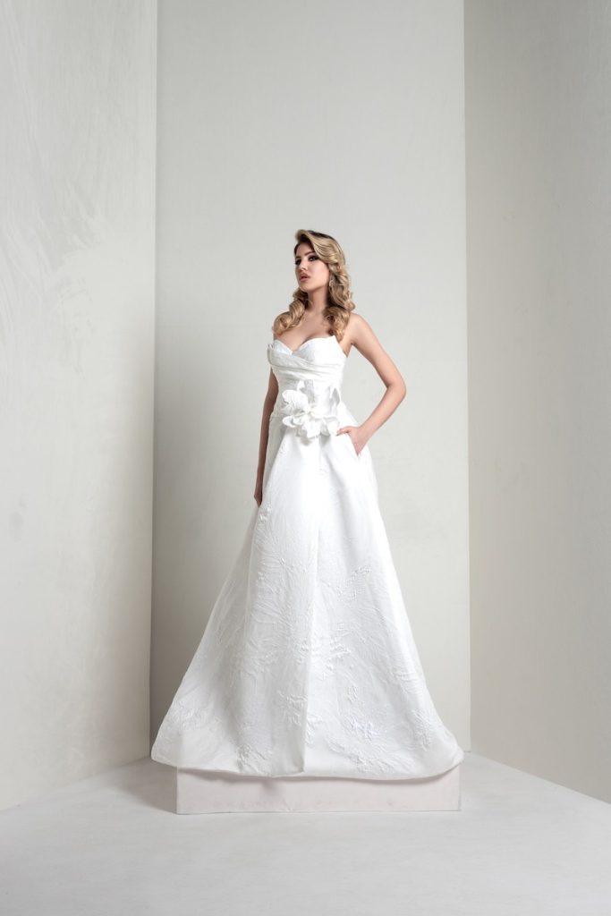 In questa foto, una modella indossa un abito della collezione sposa Markisa 2026 ad A in taffetà e maxi fiore in vita