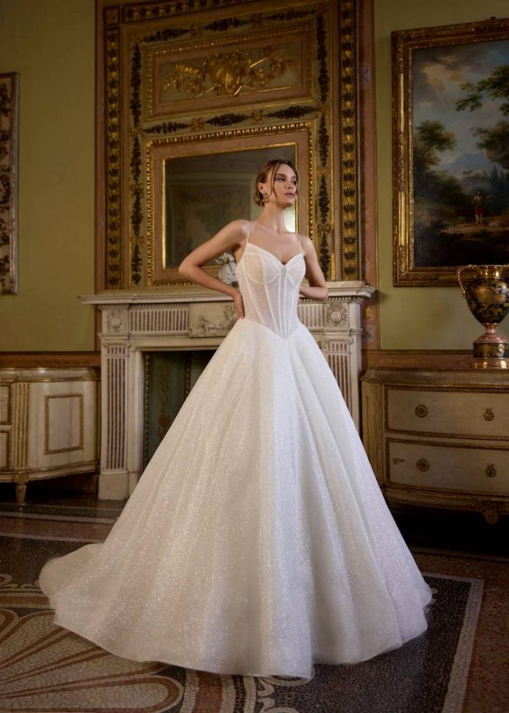 In questa foto, una modella indossa un abito da sposa principessa con bustier Randy Fenoli Bridal 2026