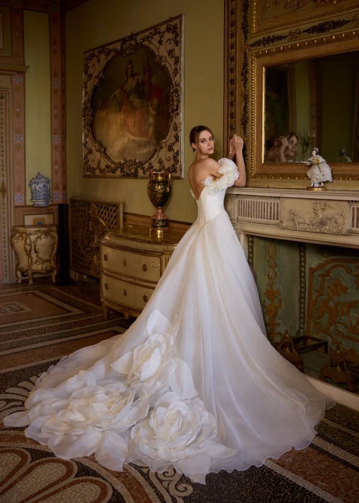 In questa foto, una modella indossa un abito da sposa ampio con maxi camelie 3D Randy Fenoli Bridal 2026