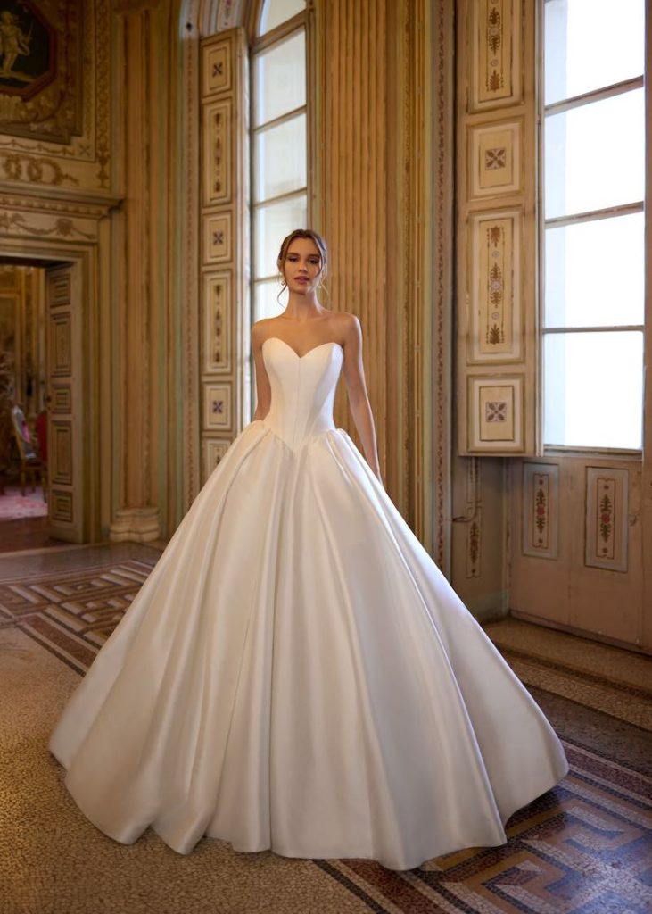 In questa foto, una modella indossa un abito da sposa principessa in mikado Randy Fenoli Bridal 2026