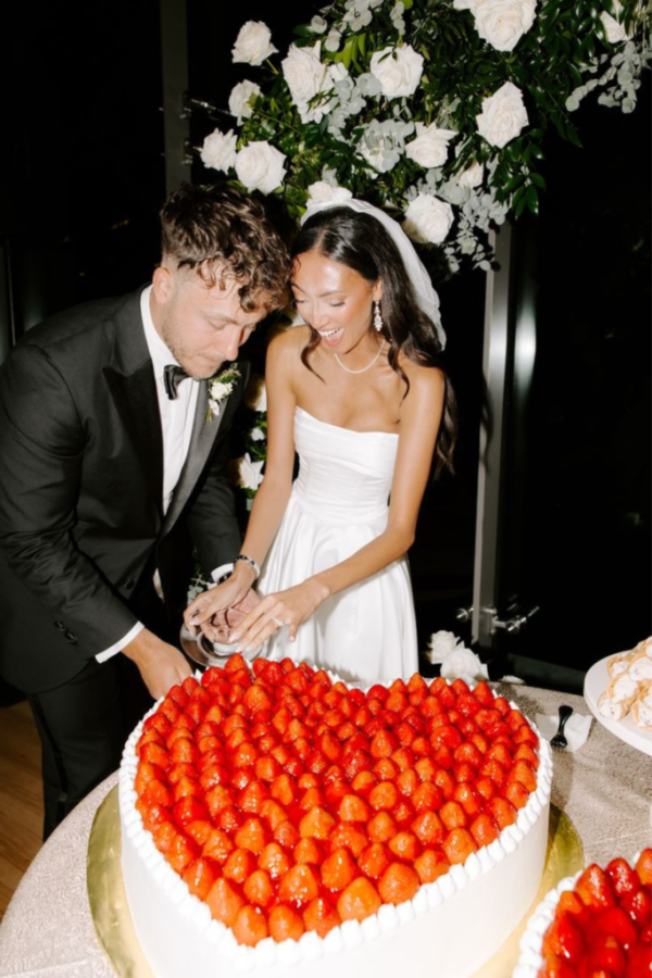 In questa foto una coppia di sposi taglia la torta di matrimonio a cuore