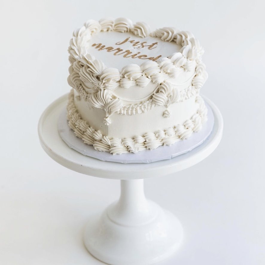 In questa foto una torta di matrimonio a forma di cuore con su scritto Just Married. La wedding cake è total white