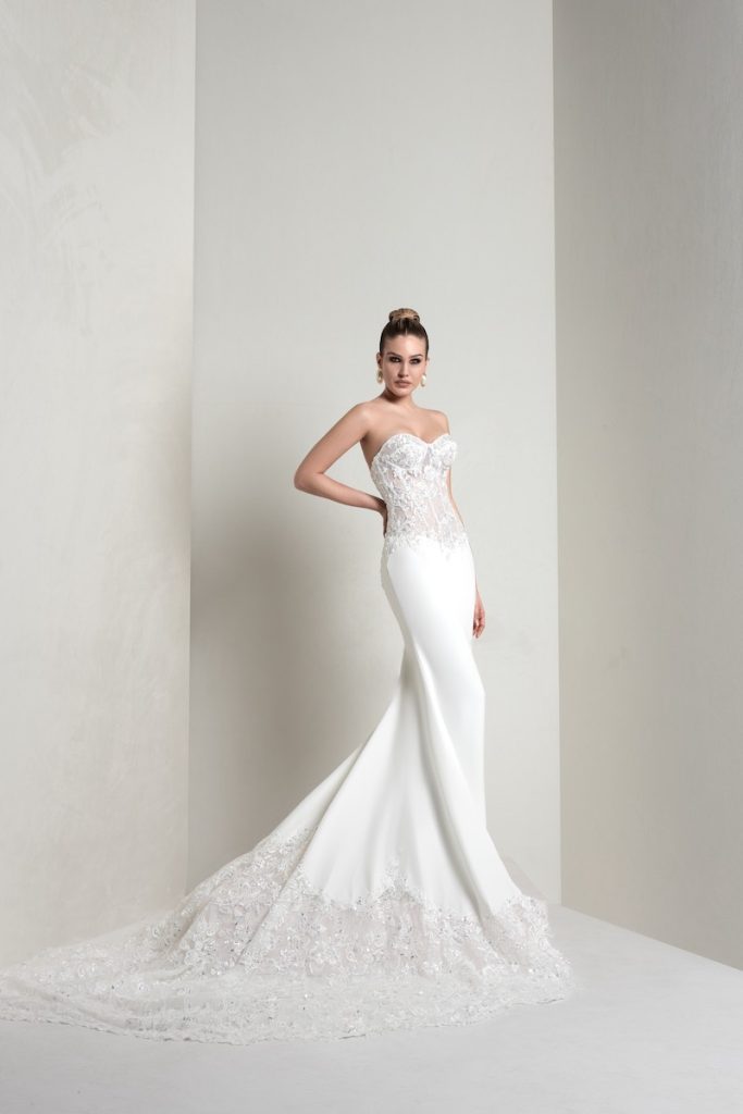 In questa foto, una modella indossa un abito della collezione sposa Markisa 2026 a sirena in tessuto combinato di pizzo e crepe georgette con bustier steccato, scollo a cuore e maxi strascisco