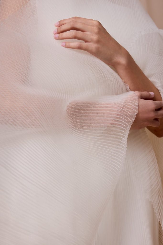 In questa foto, il dettaglio di una modella indossa un abito da sposa scivolato in tulle plissé della collezione sposa Nagae 2026