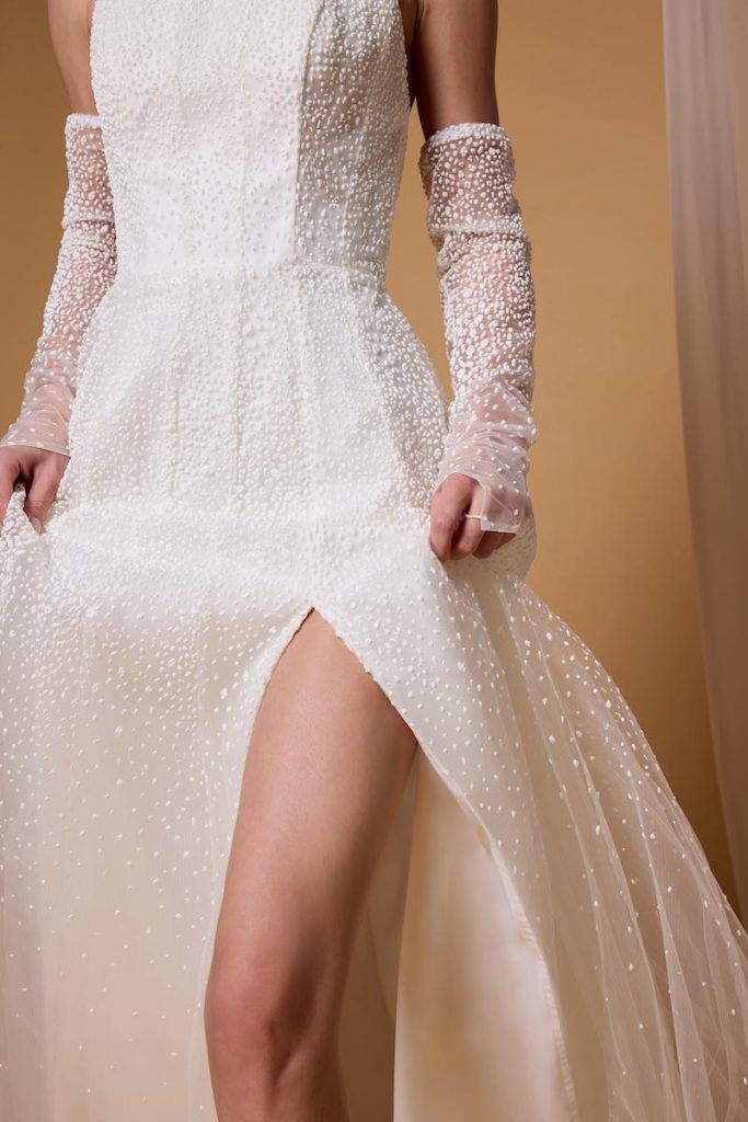 In questa foto, il dettaglio dei manicotti di una modella che indossa un abito da sposa scivolato in tulle e perline della collezione sposa Nagae 2026