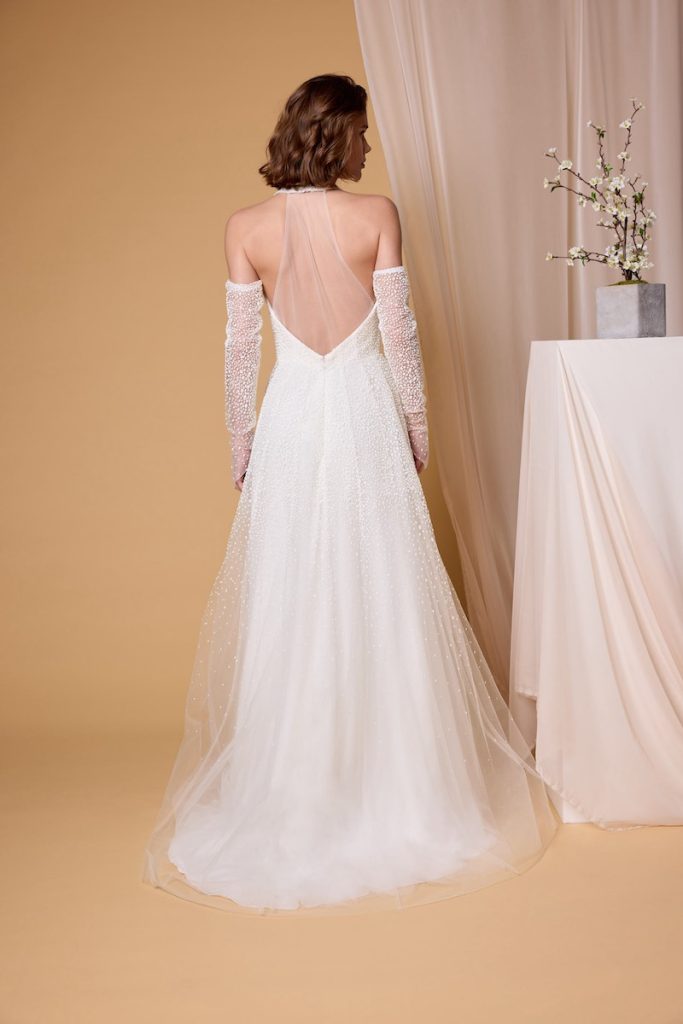 In questa foto, una modella inquadrata di spalle che indossa un abito da sposa scivolato in tulle e perline della collezione sposa Nagae 2026