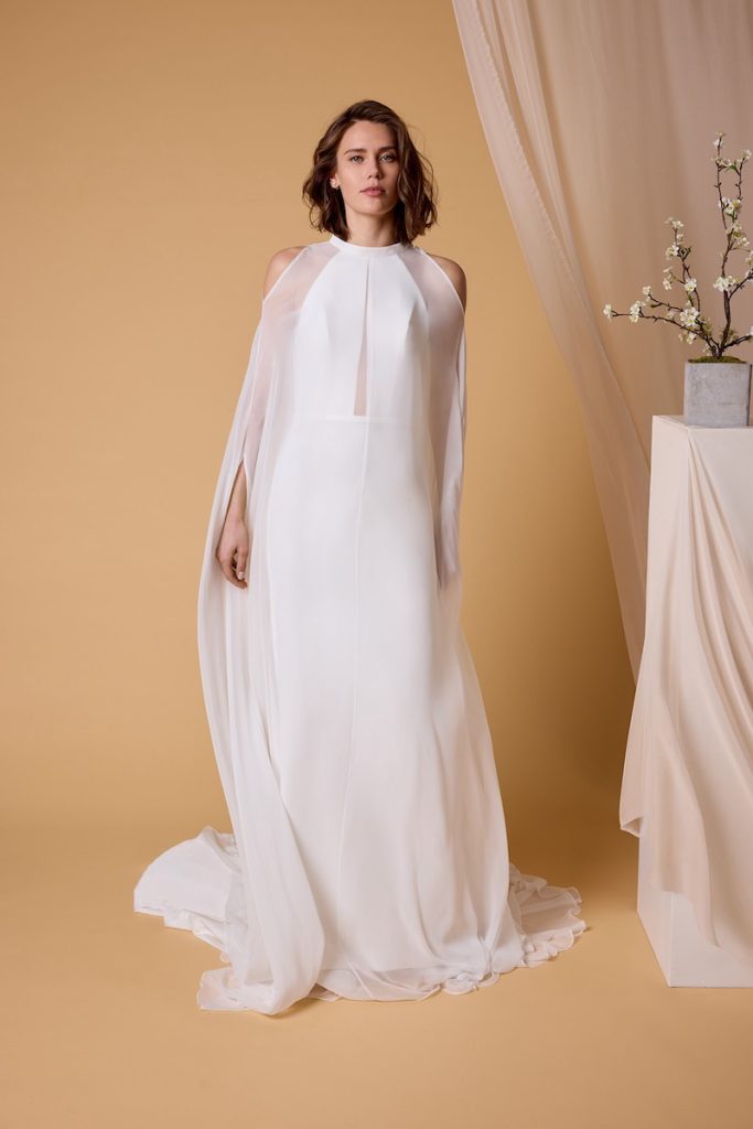 In questa foto, una modella che indossa un abito da sposa scivolato in satin triacetato con mantello in chiffon della collezione sposa Nagae 2026