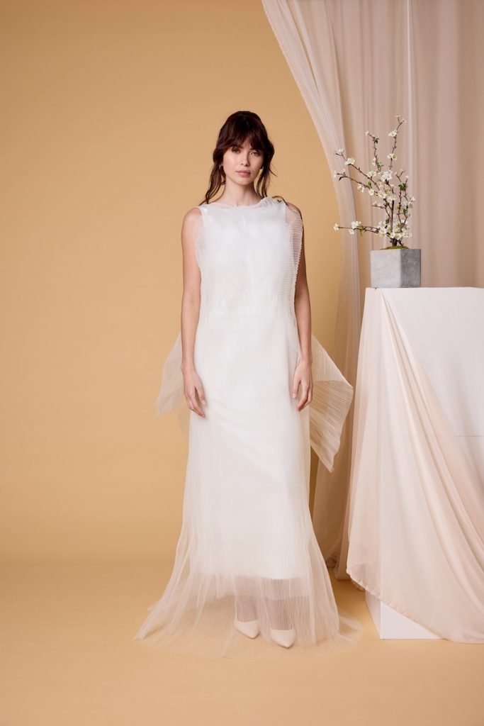 In questa foto, una modella indossa un abito da sposa scivolato in tulle plissé della collezione sposa Nagae 2026