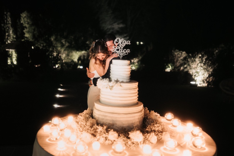 In questa foto di Federico Gritti due sposi si abbracciano dietro alla torta nuziale circondata da tea light