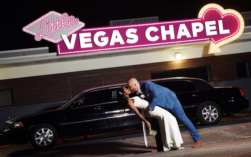 In questa foto, due sposi si baciano davanti ad una limousine parcheggiata a sua volta davanti all'ingresso della Little Vegas Chapel