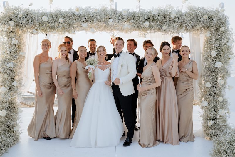 In questa foto, due sposi con le damigelle e i testimoni sotto ad un baldacchino di fiori di colore bianco al termine di un matrimonio simbolico sulla spiaggia firmato Fiorilandia