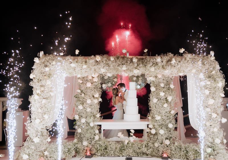 In questa foto, gli sposi si baciano dopo il taglio della torta nuziale a piani Total White sotto ad un baldacchino di rose e gypsophila bianche 