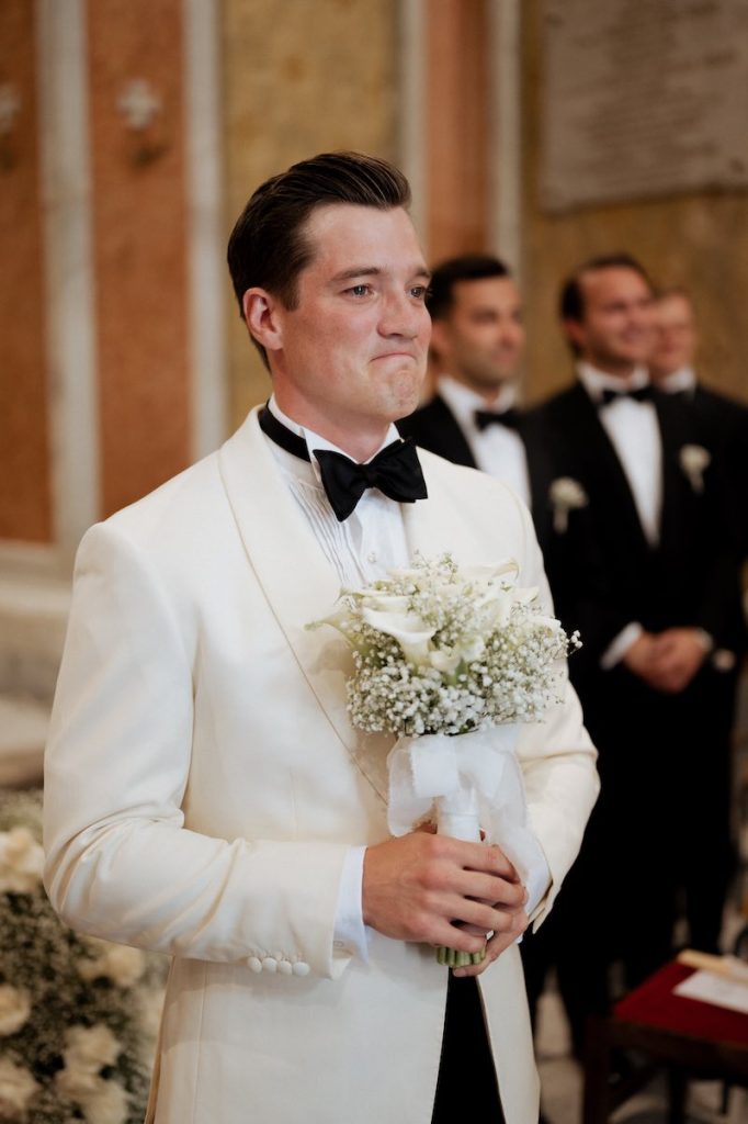 In questa foto, uno sposo aspetta emozionato la sposa all'altare con il bouquet