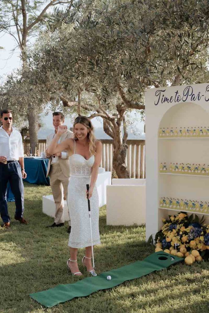 In questa foto, la sposa che gioca a golf davanti al corner del limoncello durante il loro Welcome Party firmato Fiorilandia Event Design