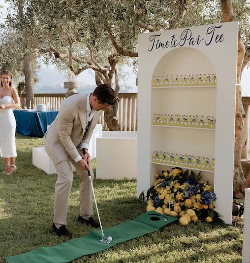 In questa foto, lo sposo che gioca a golf davanti al corner del limoncello durante il loro Welcome Party firmato Fiorilandia Event Design