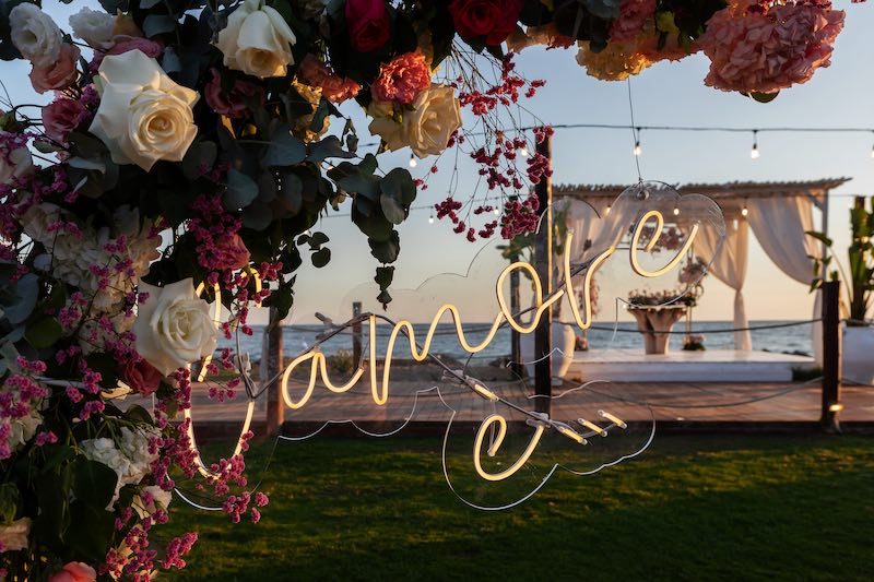 In questa foto, l'allestimento di uno di matrimoni in spiaggia al mamamare con la scritta al neon "L'amore è"