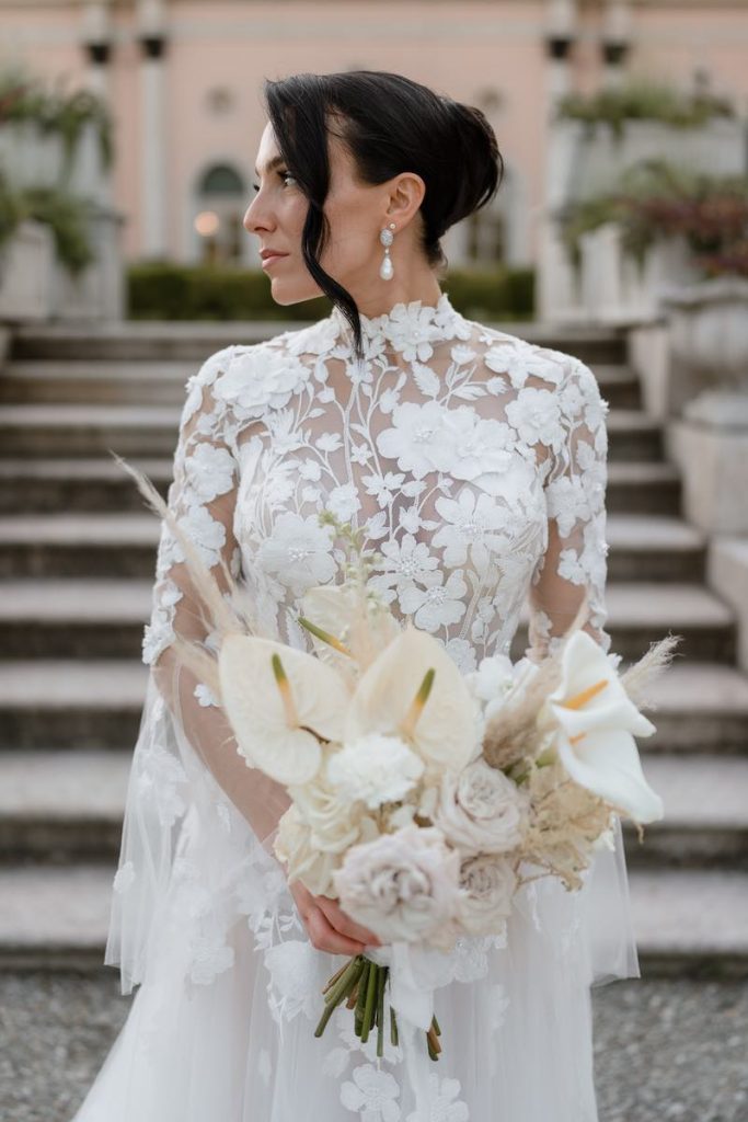 In questa foto, una sposa indossa un abito con corpetto floreale e stringe tra le mani un bouquet di fiori bianchi