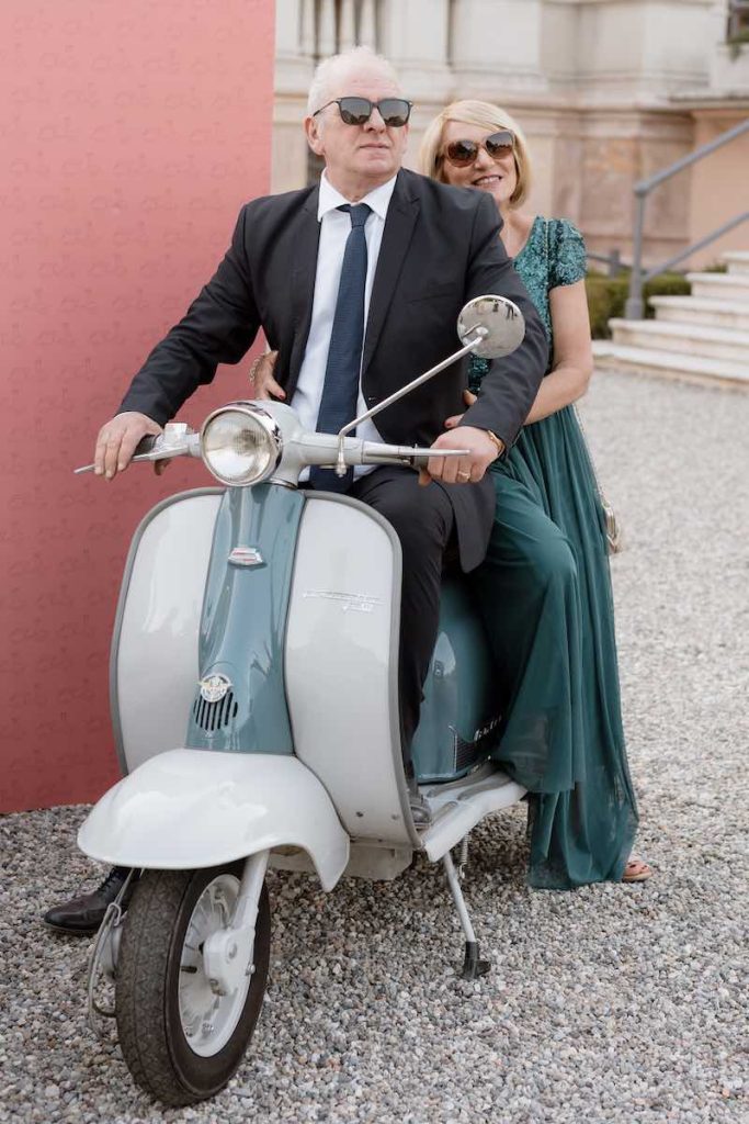 In questa foto, due invitati al matrimonio seduti su una lambretta