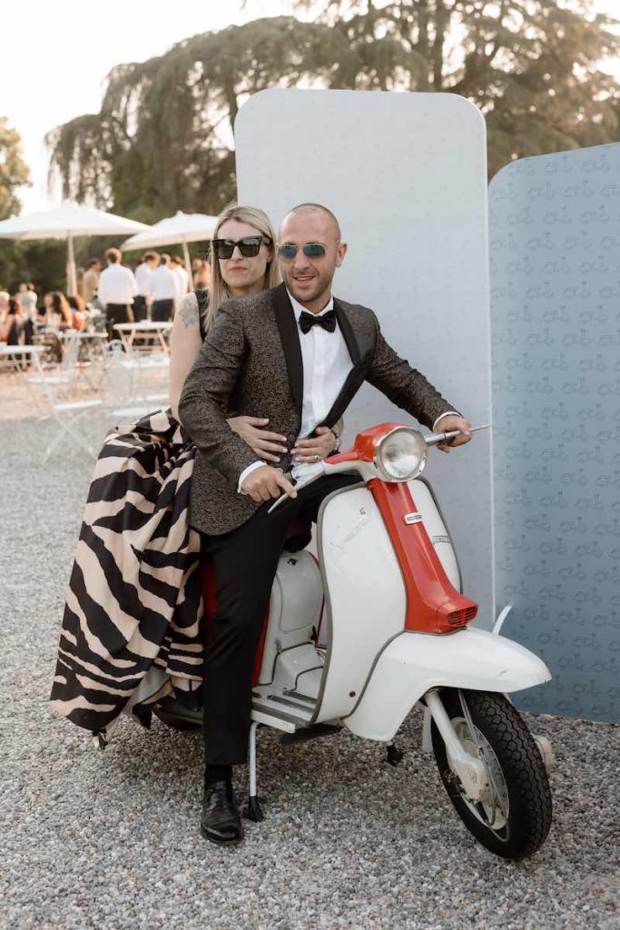In questa foto, due invitati al matrimonio seduti su una lambretta