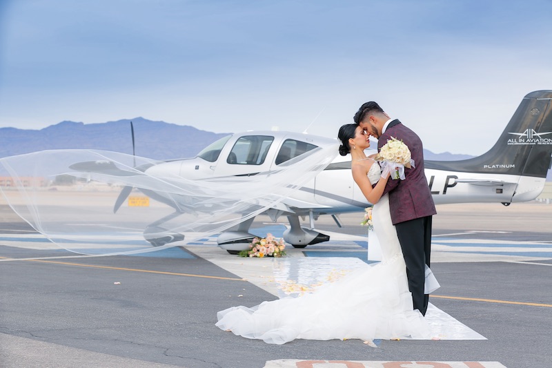 In questa foto, due sposi si abbracciano davanti ad un aereo in una pista a Las Vegas. Lei tiene nelle mani un bouquet di rose di colore bianco