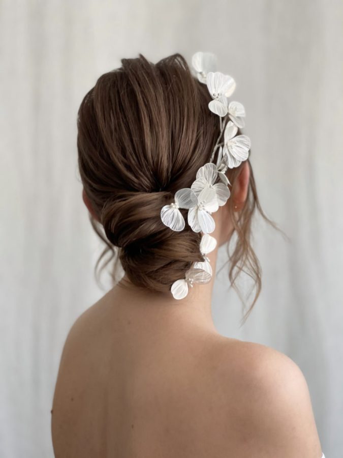 in questa foto si vede un'acconciatura sposa capelli medi acconciati con un raccolto basso con ciocche libere, la sposa ha i capelli color castano e per per impreziosire l'acconciatura ha usato decorazioni floreali argentate