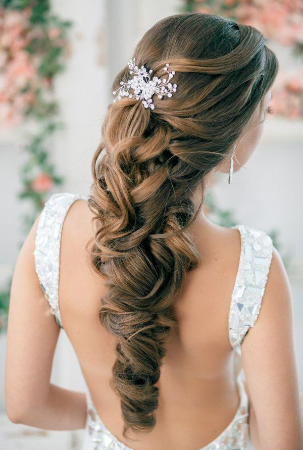 in questa foto si vede un'acconciatura sposa capelli lunghi acconciati con un raccolto con treccia impreziosita da un fermaglio gioiello, la sposa ha i capelli castani