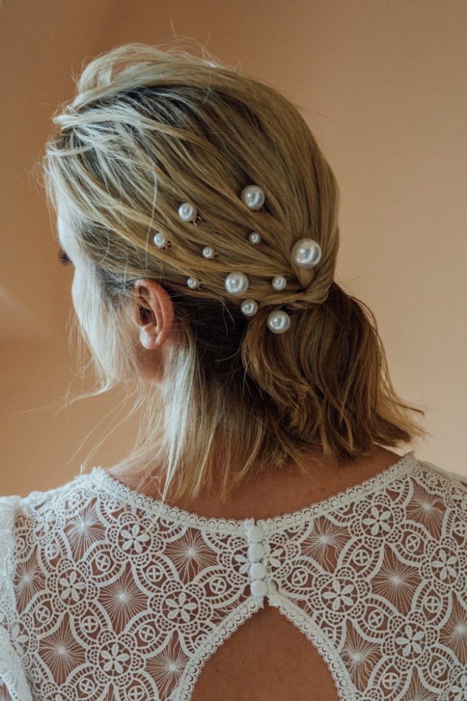 in questa foto si vede un'acconciatura sposa capelli corti color biondo cenere acconciati con un elegante mezzo raccolto impreziosito da forcine con perline