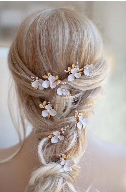 in questa foto si vede un'acconciatura sposa capelli lunghi acconciati con un raccolto con treccia impreziosita da forcine gioiello con motivo floreale la sposa ha i capelli biondi
