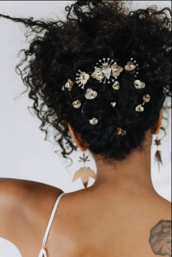 in questa foto si vede un'acconciatura sposa capelli afro raccolti dietro la nuca. l'acconciatura impreziosita da fermagli dorati