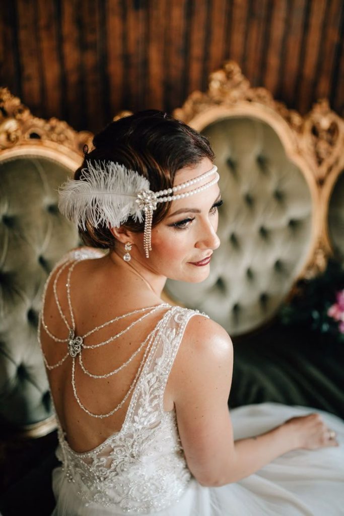 in questa foto si vede un'acconciatura sposa capelli corti con acconciatura tipica degli anni 20. il look è impreziosito da una tiara di perle e piume