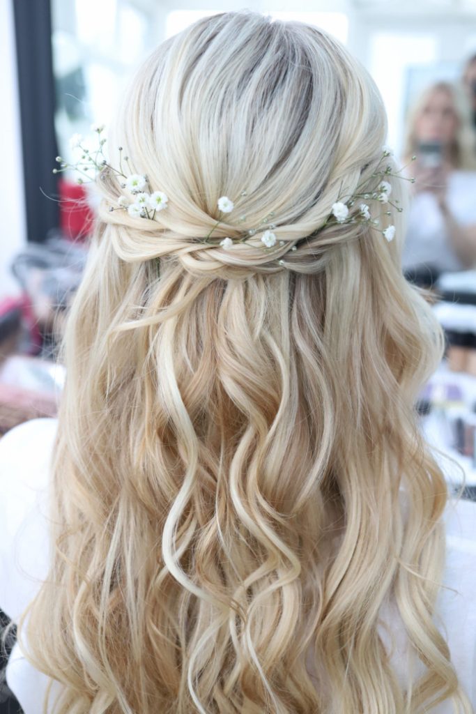 in questa foto si vede un'acconciatura sposa capelli medi acconciati con un mezzo raccolto con treccia, la sposa ha i capelli color biondo platino e per per impreziosire l'acconciatura ha usato decorazioni floreali