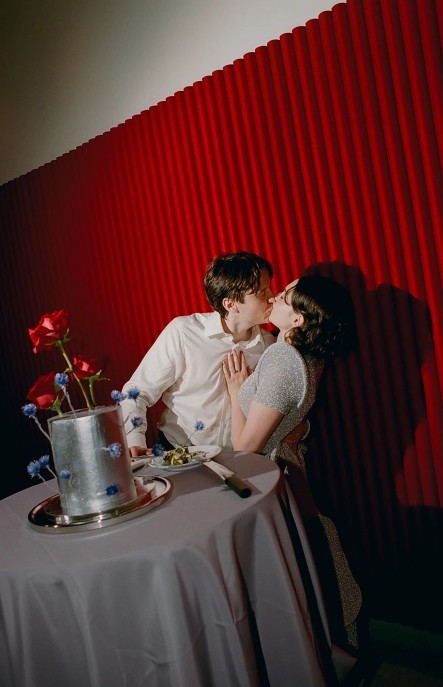 In questa foto che mostra Quale torta scegliere per il matrimonio" si vede una coppia che si bacia davanti la torta nuziale. La torta è di colore argentato con decorazioni floreali in 3D
