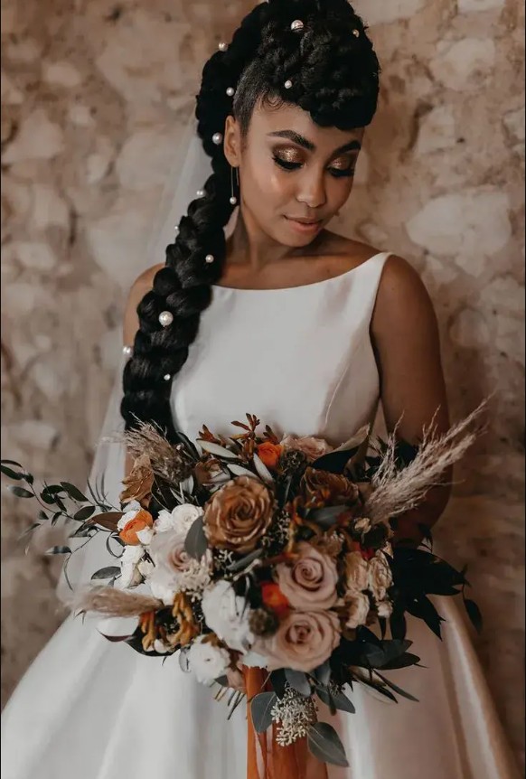in questa foto si vede un'acconciatura sposa capelli lunghi acconciati con un raccolto con treccia impreziosita da fermagli con perline la sposa ha i capelli castano molto scuro