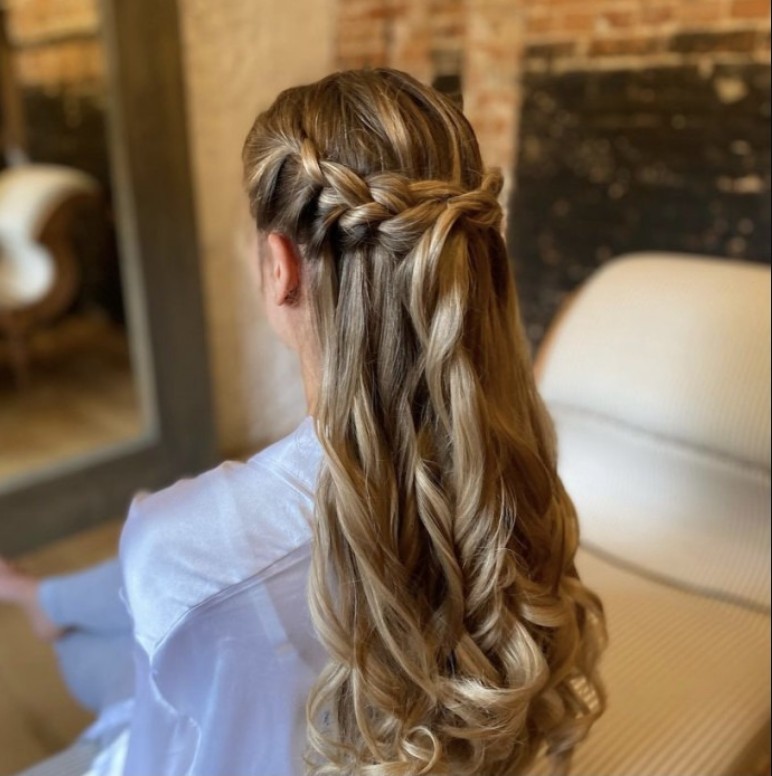 in questa foto si vede un'acconciatura sposa capelli lunghi acconciati con un raccolto con mezza treccia, la sposa ha i capelli biondi